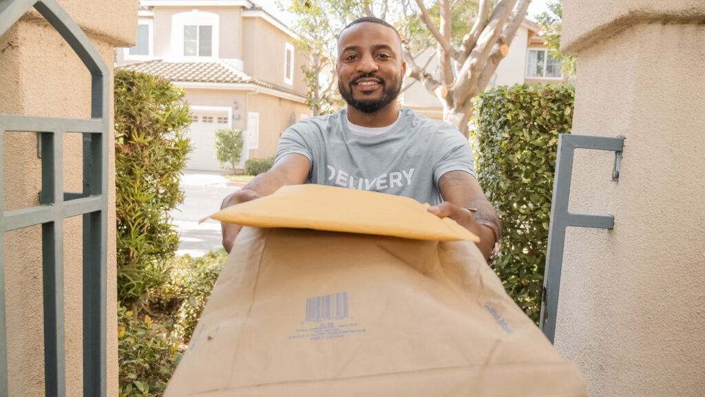 African American delivery man smiling while handing over parcels outdoors.